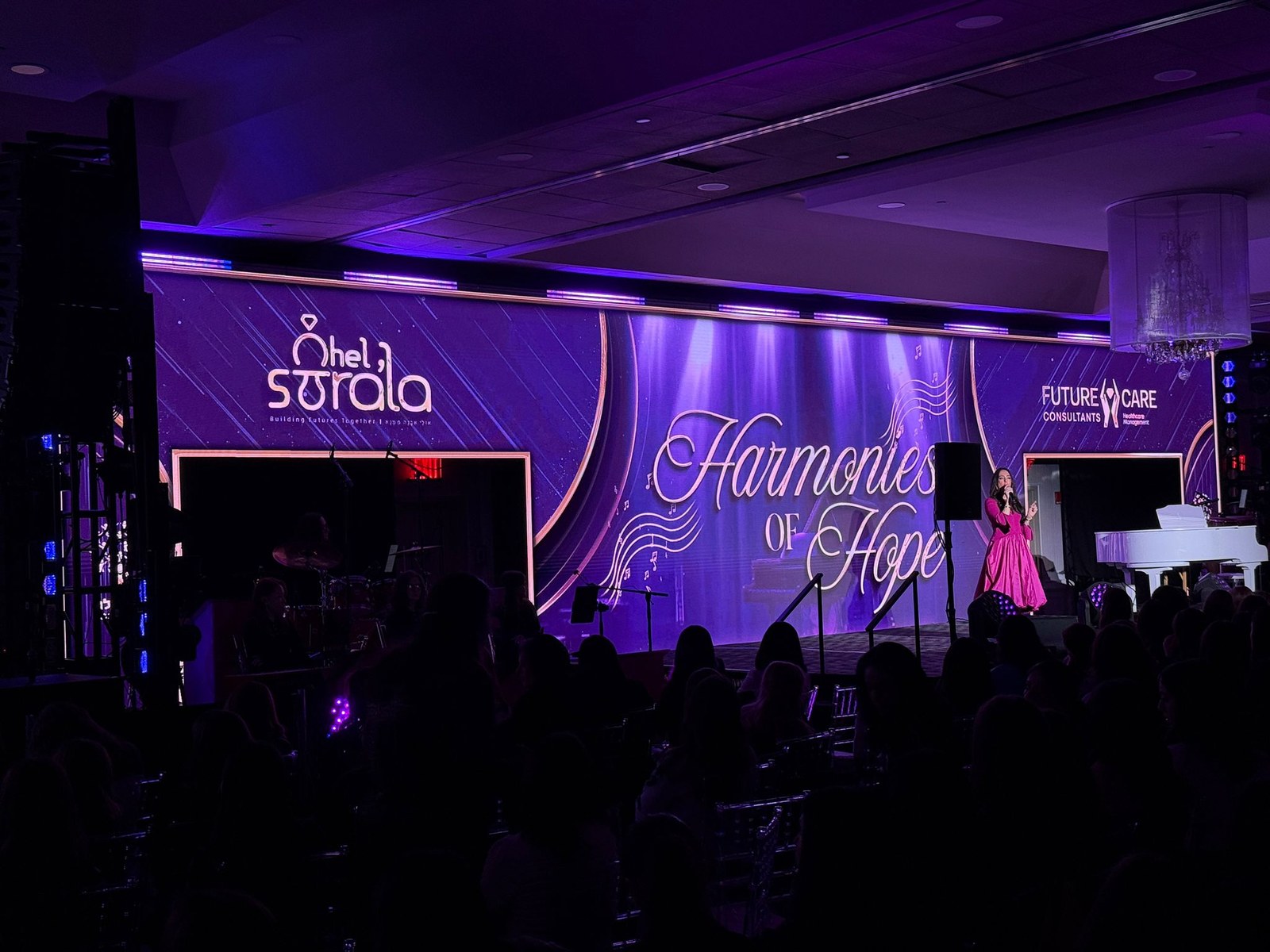 Wide violet stage backdrop with script lettering reading Harmonies of Hope