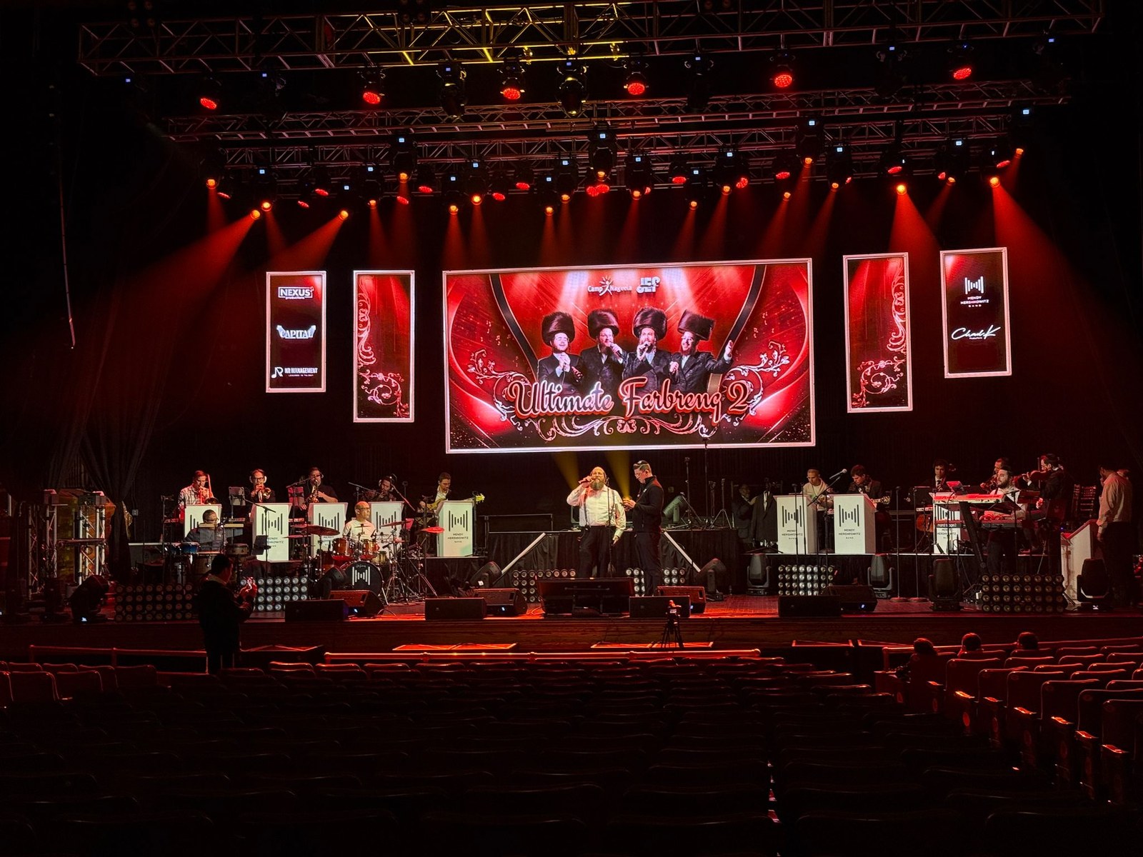 Concert stage washed in red with a wide central screen and side banners