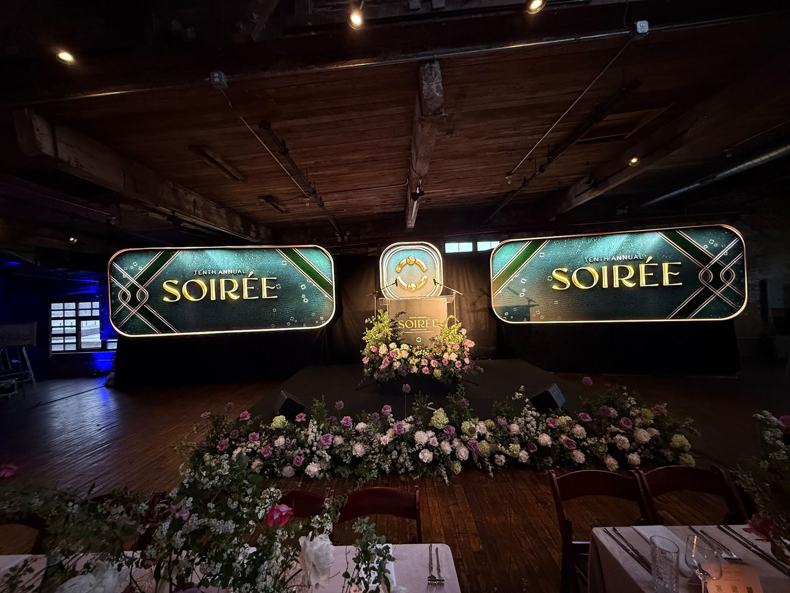Emerald and gold art-deco screens reading Tenth Annual Soirée in a timber loft