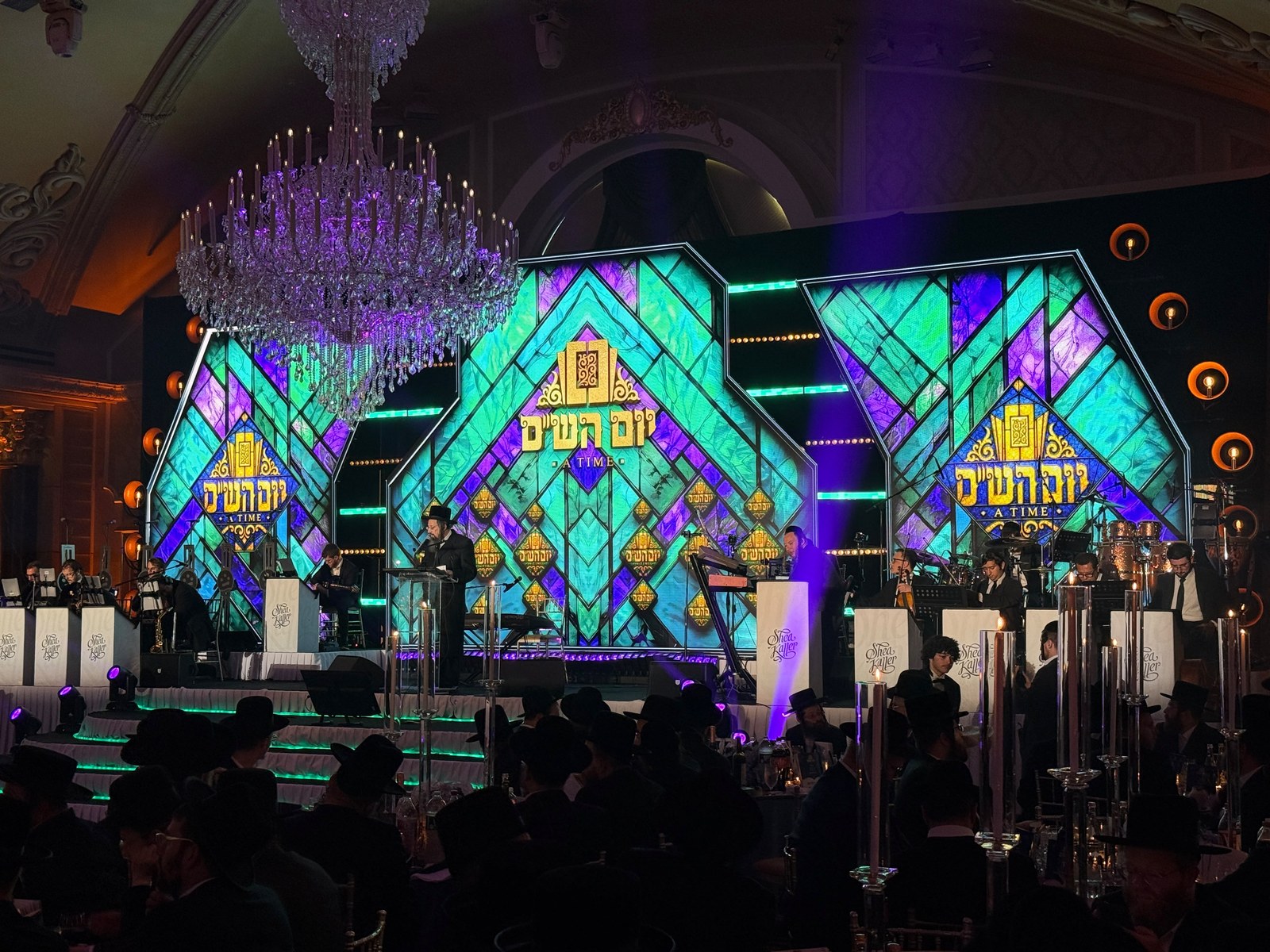 Stage backdrop of illuminated stained-glass panels in teal, violet and gold